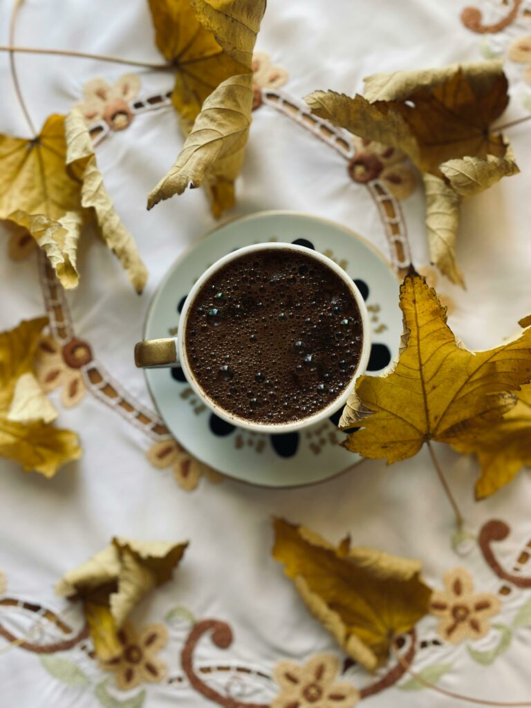 Top view of hot chocolate amidst autumn leaves on a decorative tablecloth.