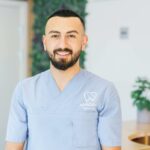 A friendly dentist in scrubs standing in a bright, modern dental office, ready to assist patients.